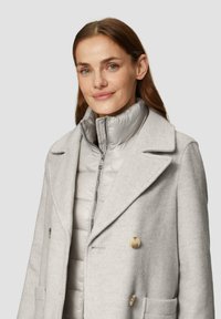 Hellgrauer Peacoat mit schmalem Kragen und doppelt geknöpften Knöpfen, über einem hellgrauen Pufferjacke mit hohem Kragen und Reißverschluss getragen.
