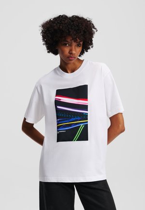 Witte katoen t-shirt met een grote zwarte afbeelding met kleurrijke, abstracte lijnen in roze, blauw, geel en groen. Korte mouwen.