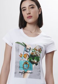 Camiseta blanca de manga corta con un gráfico de un bolso y flores, con estampados coloridos y la palabra "influencer" en negro.