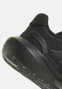 Svart sportskor med överdel av nätmaterial, texturerad detalj på hälen och en tjock, gummisula med greppgropar.