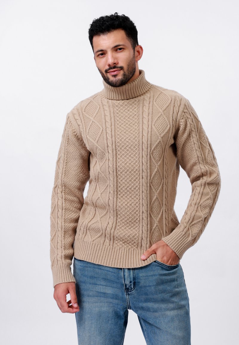 Pull en tricot beige avec un col montant. Présente un motif en losanges texturé et des poignets côtelés. Associé à un jean bleu.