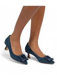 Tacchi in suede blu navy con punta affilata, caratterizzati da un accento quadrato gioiello sul vamp e un tacco basso a blocco.