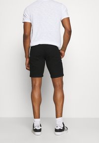 Shorts de mezclilla negra con puños enrollados, combinados con una camiseta gris jaspeada. El modelo lleva calcetas deportivas blancas y zapatillas deportivas negras.