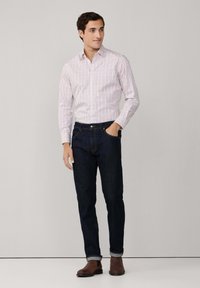 Chemise blanche à motif à carreaux rouges et bleus, associée à un jean en denim sombre. Avec des manches retroussées et des bottes en cuir marron.
