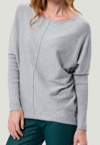 Pull long à manches longues gris clair avec un col rond et une coupe décontractée, présentant des poignets côtelés et un détail de couture diagonale.