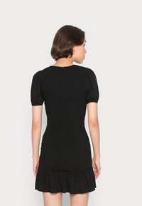 Vestido preto com mangas bufantes, tecido texturizado, corpete ajustado e bainha franzida. Apresenta um decote em forma de lágrima nas costas com um pequeno fecho de zip.