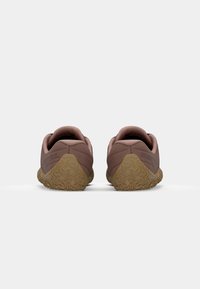 Chaussures de sport marron avec une semelle en caoutchouc texturé, des talons arrondis et un col rembourré. Marque affichée au niveau du talon.