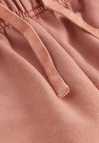 Pantalones deportivos de color rosa claro con tela texturizada, cintura elástica y cordón plano. Vista en primer plano que muestra los detalles de las costuras.