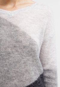 Maglione morbido lavorato a maglia con un motivo diagonale grigio e bianco, dotato di scollo a V e maniche lunghe, indossato sulla parte superiore del corpo di una persona.