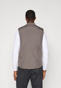 Gilet senza maniche marrone realizzato in un tessuto leggero e morbido, con un colletto alto. Il design presenta una cucitura orizzontale sulla schiena.