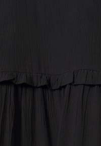 Schwarzer Stoff mit einer zerknitterten Textur und einem gerafften Rüschendetail, das einen gestuften Effekt erzeugt.