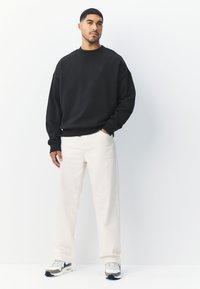 Fekete pulóver lehajtott vállal, krémszínű, széles szárú nadrággal párosítva. A lábbeli fehér és szürke dizájnnal, fekete részletekkel.