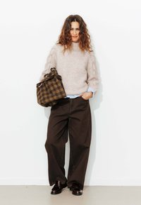 Pull en tricot texturé rose clair avec des manches bouffantes ; associé à un pantalon large marron foncé et un sac à carreaux marron. Des chaussures sombres complètent le look.
