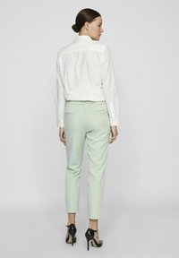 Chemise blanche à col et pantalon tapered vert menthe, doté d'une taille élastique, de poches arrière et de chaussures à talons hauts noires.