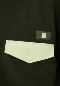Veste en polaire vert foncé avec une surface texturée. Présente un rabat de poche vert clair avec un bouton-pression et une petite étiquette logo.