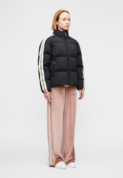 Μαύρο μπουφάν τύπου puffer με κρεμ ρίγες στα μανίκια, τσέπες με φερμουάρ· συνδυασμέ νο με απαλό ροζ βελούδινο παντελόνι με φαρδιά πόδια και άσπρα παπούτσια.