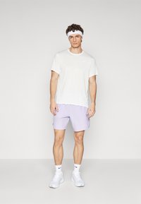 White textured short-sleeve shirt, light purple shorts, and white sneakers. Headband adds contrast; Nike logo on shirt and shorts.