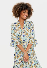 Rochie florală cu o bază de culoare bleu deschis, având motive vibrante de albastru și aur. Mânecile volan sunt detaliate, iar decolteul în formă de V adaugă un plus de eleganță.