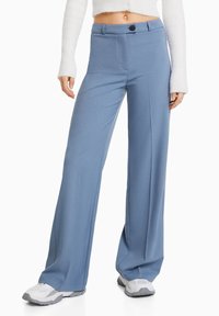 Light blue wide-leg trousers with a smooth texture, featuring a single button closure and front pockets. Paired with gray athletic shoes.