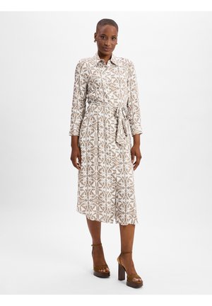 Light beige dress with a white ornate pattern, collar, three-quarter sleeves, and a tied waist. Paired with brown strappy block heels.