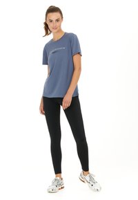 Blå sports T-shirt med korte ærmer og rund halsudskæring. Sorte leggings og sølvfarvede løbesko med orange detaljer fuldender outfittet.