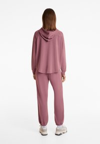 Rosa Kapuzenpullover und passende Jogginghose aus weichem Stoff, mit lässiger Passform, elastischen Bündchen und Kapuze mit Kordelzug. Sneaker runden den Look ab.