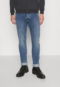 Mörkgrå zip-up sweatshirt, ljusblå denimjeans, rullade ärmslut och svarta snörkängor. Avslappnad outfit med kontrasterande färger.