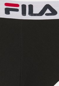 Crne atletske gaće s bijelim pojasom na kojem je "FILA" logo u tamnosivoj boji i crvenim detaljima. Materijal izgleda glatko i rastezljivo.