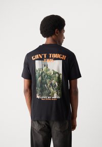 Schwarzes Baumwoll-T-Shirt mit einer großen Kaktusgrafik auf der Rückseite, darüber in orangefarbener Schrift der Text "DAS DARF MAN NICHT ANFASSEN".