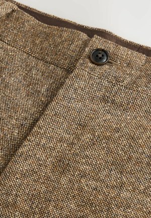 Ruskea tweed-kangas, jossa on teksturoitu kudonta, musta nappi ja ruskea vyötärö. Väri on yleisesti ottaen hienovaraisilla vaihteluilla.