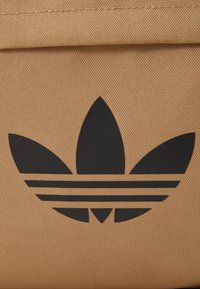 Oranžová textúrovaná tkanina s čiernym logom Adidas trefoil, ktoré obsahuje tri pruhy. Dizajn je výrazný a jasne zobrazený na materiáli.
