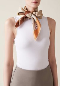 Top in cotone bianco aderente abbinato a una sciarpa di seta patterned legata a fiocco attorno al collo, con tonalità di beige, marrone e arancione.
