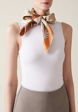 Top in cotone bianco aderente abbinato a una sciarpa di seta patterned legata a fiocco attorno al collo, con tonalità di beige, marrone e arancione.