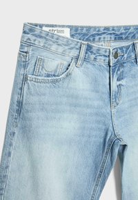 Jeans di denim azzurro chiaro con bottoni frontali, passanti per cintura e tasche frontali cucite, mostrati dalla vita fino a metà coscia su uno sfondo bianco.