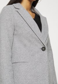 Grijze blazer van wolmix met een rever, enkele zwarte knoopsluiting en klepzakken. Zachte textuur met een getailleerde pasvorm.