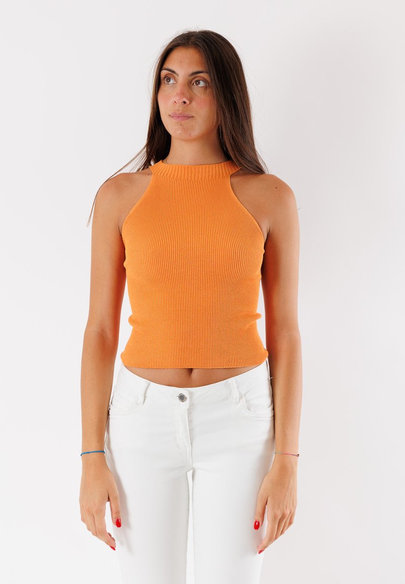 Top corto a righe arancione con un colletto alto e aperture laterali, abbinato a jeans bianchi. Texture liscia e design aderente.
