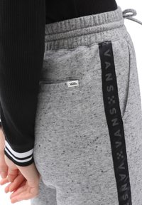 Graue Sweatpants aus strukturiertem Stoff, mit einem schwarzen Vans-Logo-Streifen an der Seite und einem kleinen Etikett auf der Rückentasche.
