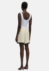 Witte tanktop gecombineerd met lichtbeige shorts met een zwart, gegolfd zoom. Soepele stof met een elastische tailleband.