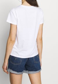 Vit bomullst-shirt med korta ärmar, med en rund halsringning. Matchad med denimshorts, lätt slitna i fållen.