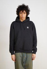 Μαύρο φούτερ από βαμβάκι με καγκουρό τσέπη και κουκούλα με κορδόνι, με μικρό λευκό λογότυπο Adidas στο στήθος. Χαλαρή εφαρμογή.