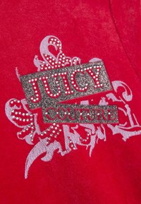 Piros bársony anyag ezüst csillámos "JUICY COUTURE" logóval és díszes fehér virágmintákkal, melyeket apró, áttetsző strasszkövek díszítenek.