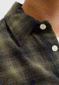 Skjorte med knaplukning, der har et ternet mønster i mørkegrøn og sort. Blødt stof med struktureret krave og hvide knapper.
