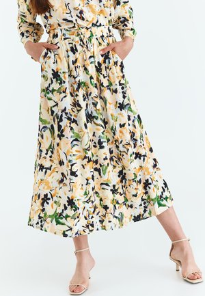 Robe à motifs floraux avec une taille ajustable, fabriquée en tissu léger. Les couleurs incluent le jaune, le vert et le noir sur un fond crème.