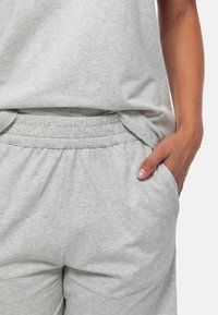 Hellgraue, weiche Jogginghose aus Baumwollmischung mit elastischem Bund, seitlichen Taschen und lockerer Passform, kombiniert mit einem passenden grauen Oberteil.