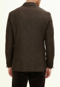 Blazer in tweed marrone con motivo a spina di pesce, rever a punta, due bottoni e un design aderente, che mostra la parte posteriore e le spalle.