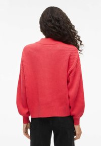 Punane kootud kampsun soonikkoes, tilkuvate õlgade ja laia, lõdva lõikega. Omadusteks ümar krae ja mansetiga varrukad.