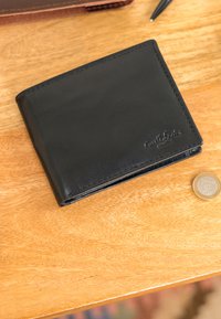 Sort læderpung præget med "Griff Leder" på et træbord ved siden af en en-euro mønt og en pen.