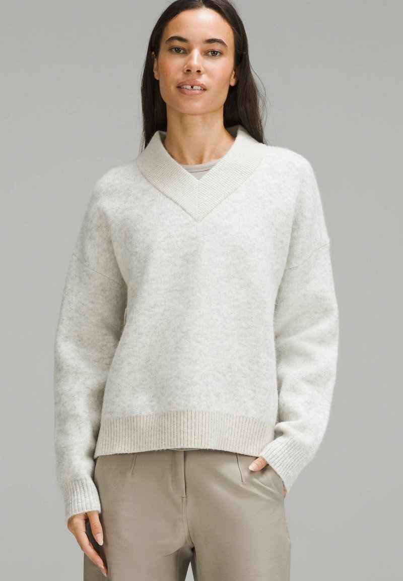 Suéter gris claro de gran tamaño, hecho de una suave tela texturizada. Presenta un escote en V y puños acanalados, con un corte holgado y dobladillo.