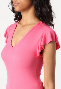 Top de color rosa con textura acanalada que presenta un escote en V y mangas cortas con volantes, destacando un diseño ajustado y una textura suave.