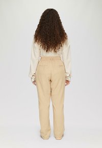 Beige linnen broek met een ontspannen pasvorm, voorzien van een hoge taille met riem en zakken. Het model draagt een lichte, gestreepte top.